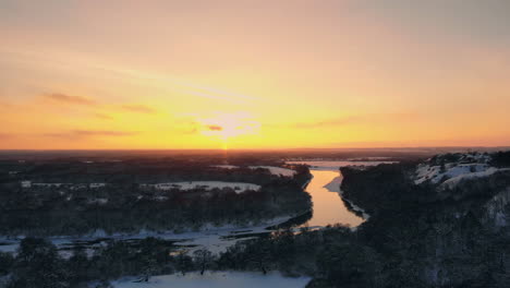 Sunset-over-frozen-river-and-evergreen-forest.-Country-highway-passing-across-water-at-winter-season.